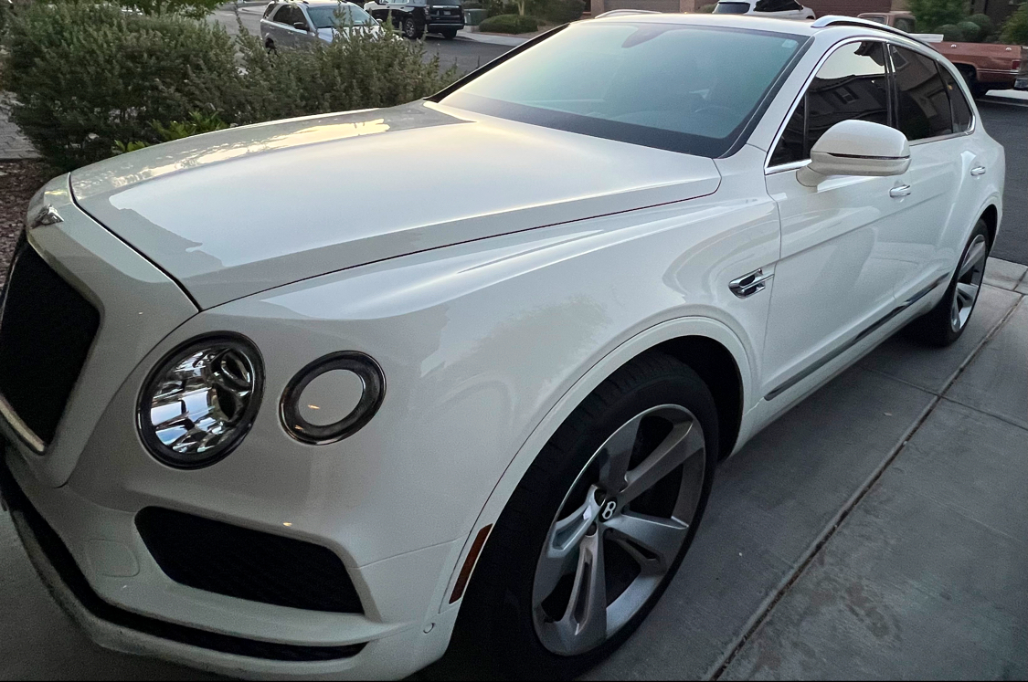 White Bentley Bentayga with tinted windows in a driveway at dusk